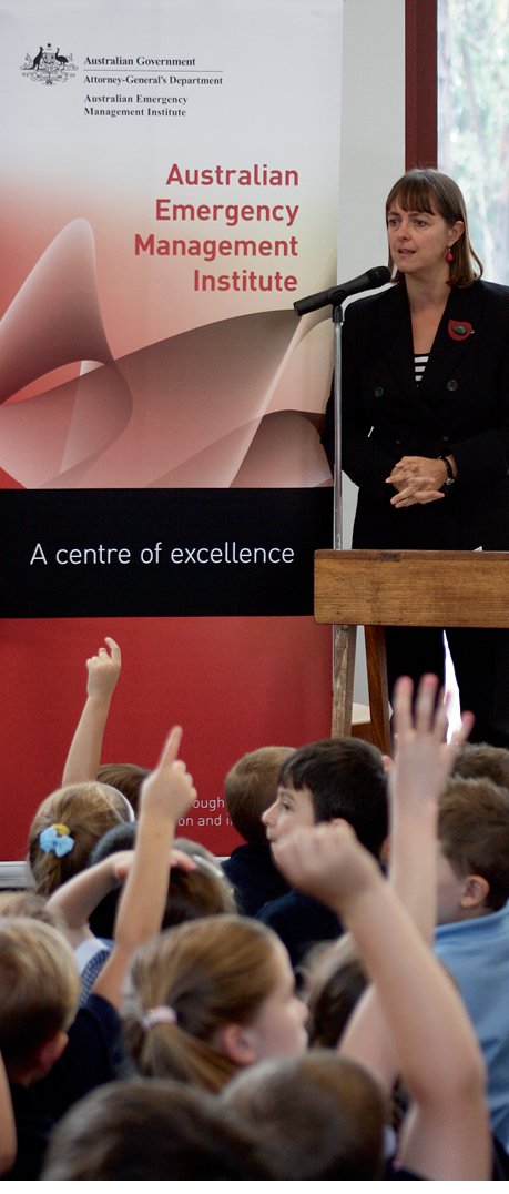 Photograph of the Hon Nicola Roxon speaking behind a podium in front of an audience of young children with raised hands
