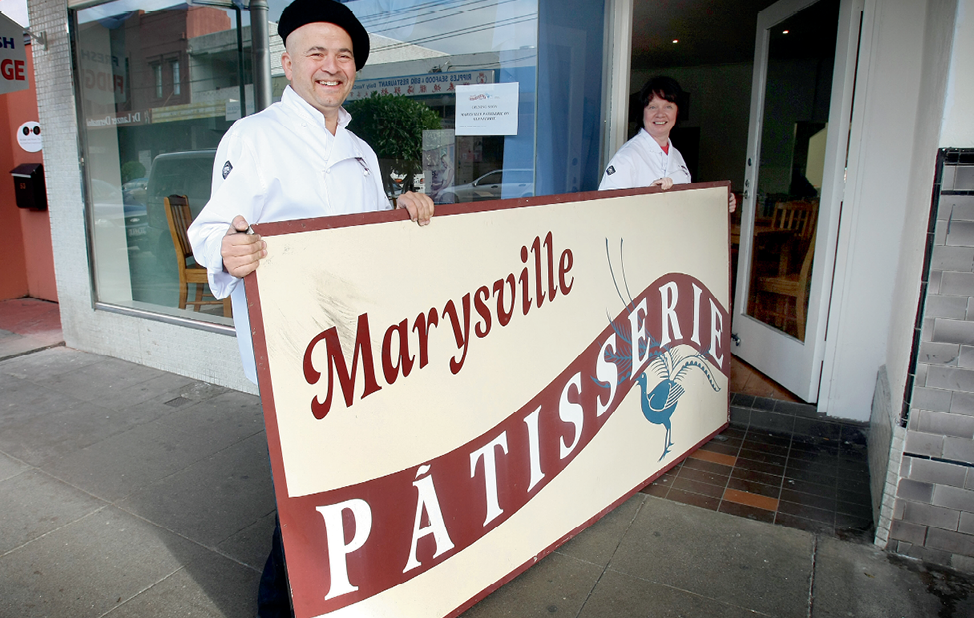 Photograph of Marysville Patisserie owners carrying the shop’s sign