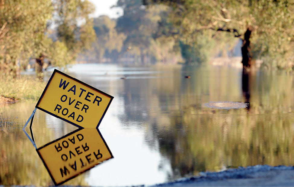 Photograph of a ‘Water over road’ hazard sign in floodwaters