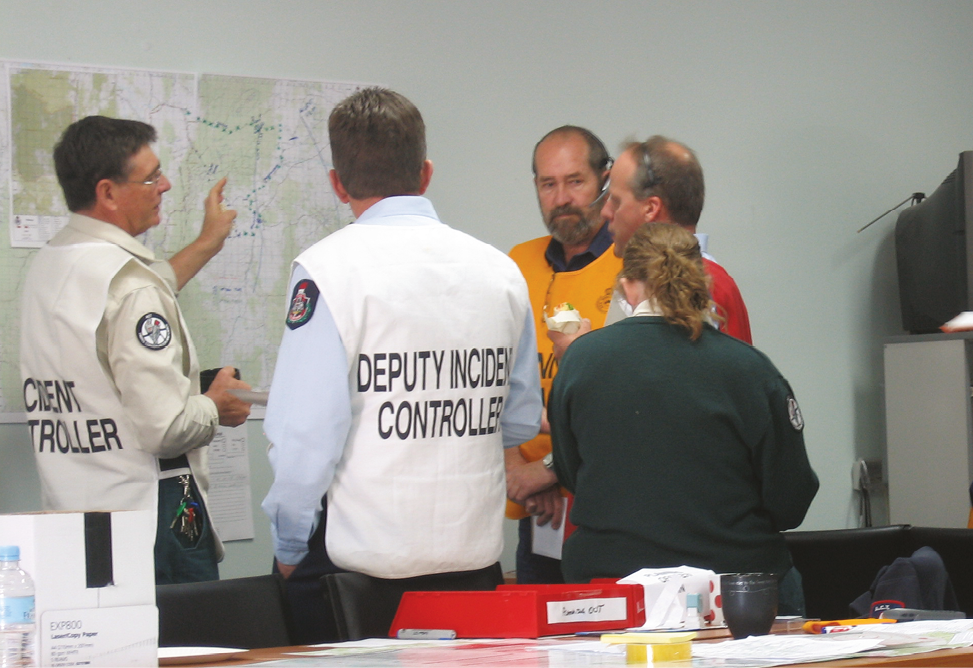 Five emergency services personnel are gathered around a wall map.
