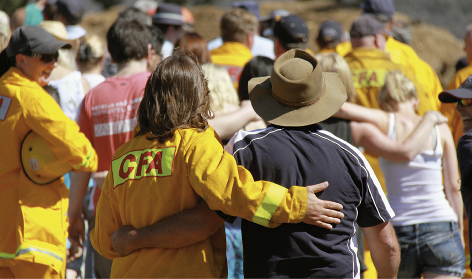 A group of men and women are walking away from the camera, some are dressed in CFA yellow uniforms, some have their arms around each other.