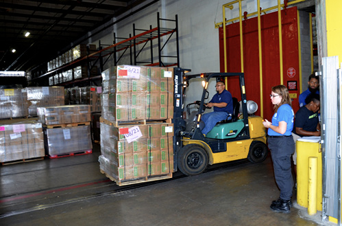Workers in a warehouse are transporting palettes of supplies with a forklift.