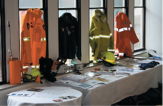 Four different emergency services jackets hanging in windows above a table covered with emergency equipment and information items