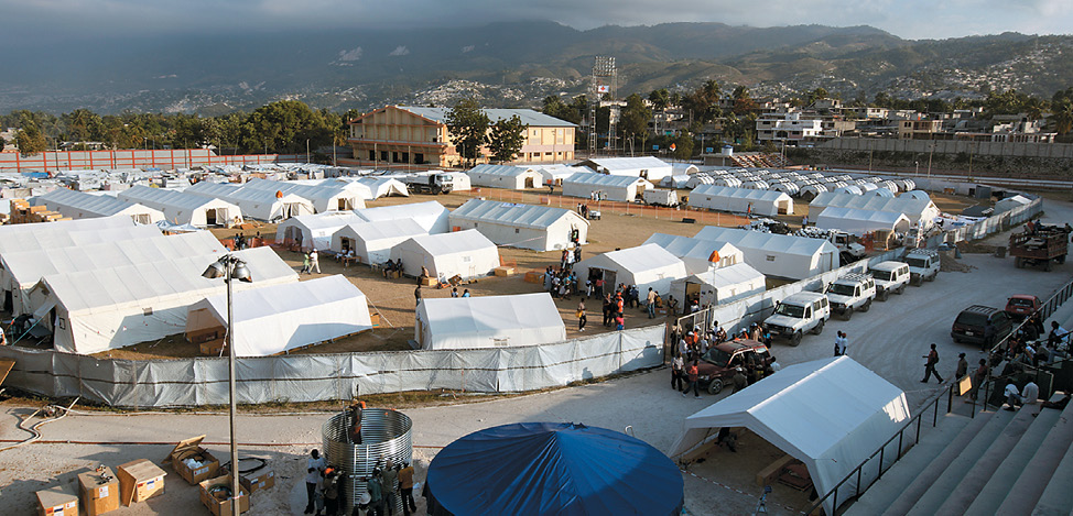 A field of organised white tents surrounded by an urban landscape