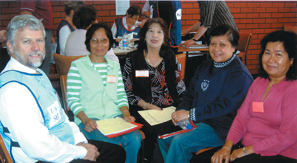 Four women of various ethnicity are sitting in a group with a middle-aged man wearing a volunteer's vest.