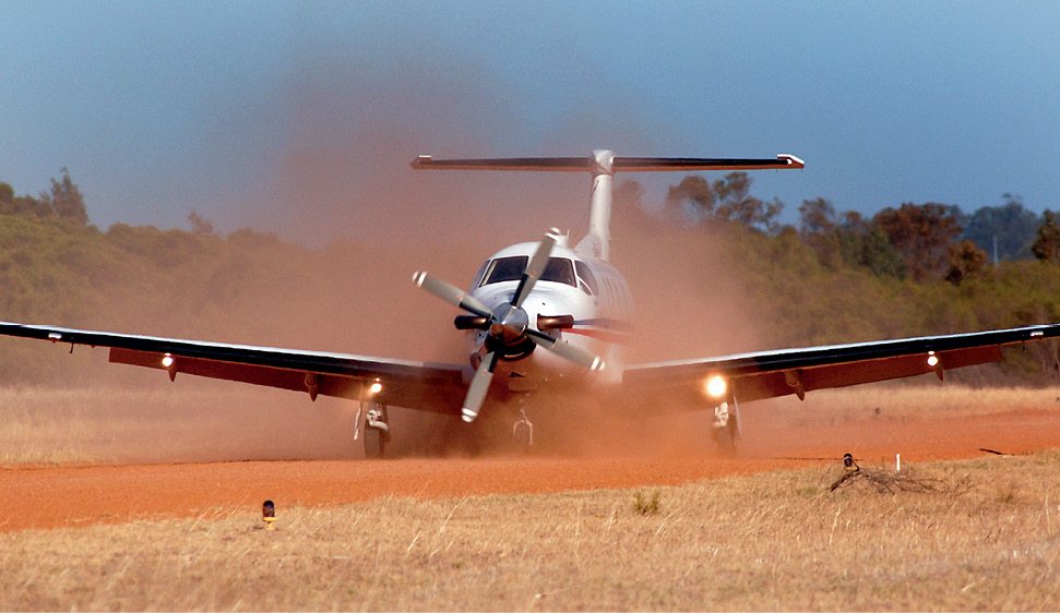 A Royal Flying Doctor Service aircraft taxis along a red-dirt airstrip with bush in the background