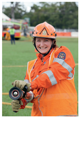 A smiling female firefighter is demonstrating how to hold a fire hose.
