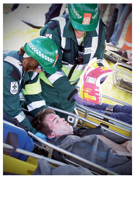 Two uniformed ambulance officers are tending to a young male patient on a gurney.