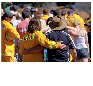 A crowd of people including a number of CFA personnel are walking with arms around each other in an outdoor setting.