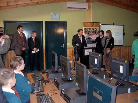 Robert McClelland is addressing a classroom of primary school students seated at computer desks. Mike Kelly and several other adults are standing around the room.