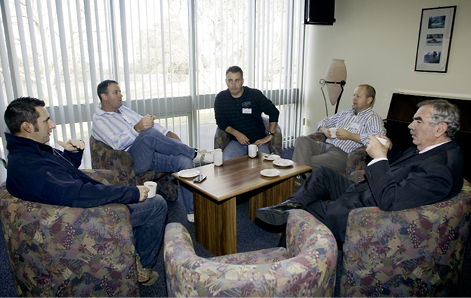 Five men sit around a coffee table in a lounge room talking and drinking coffee.