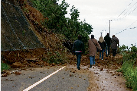 Photograph of a road blocked by fallen earth with several people walking across the fallen earth.