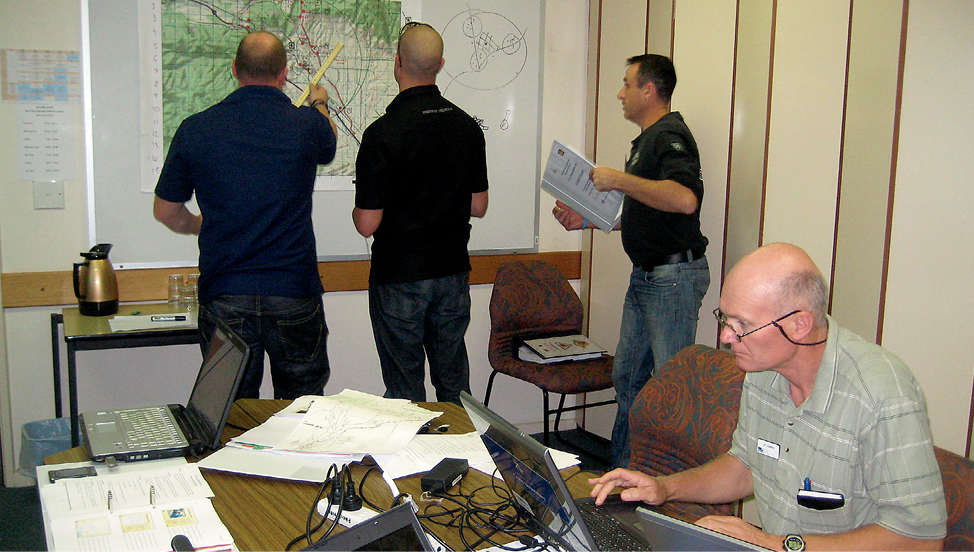 3 men assess a map while another is working at a computer.