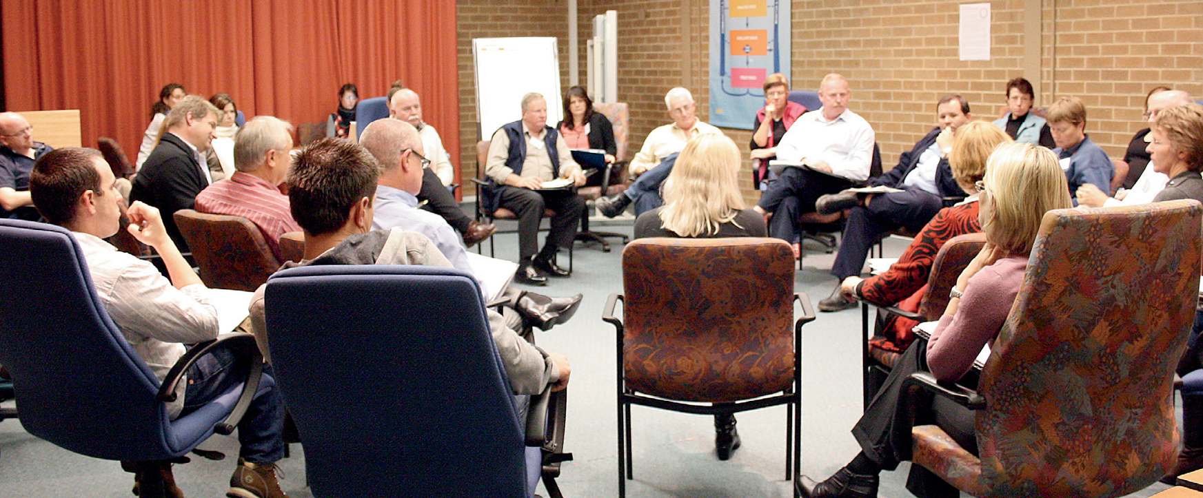 Photograph of people sitting in a large circle facing each other, discussing community engagement on the topic of hazards and disasters.