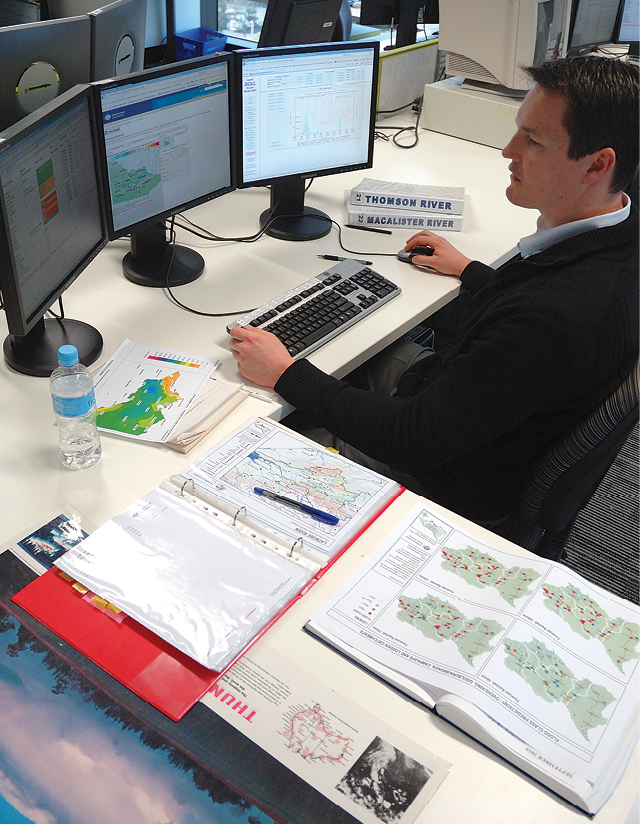 Photograph of a man looking at three computer screens. The screens show data and information about floods.