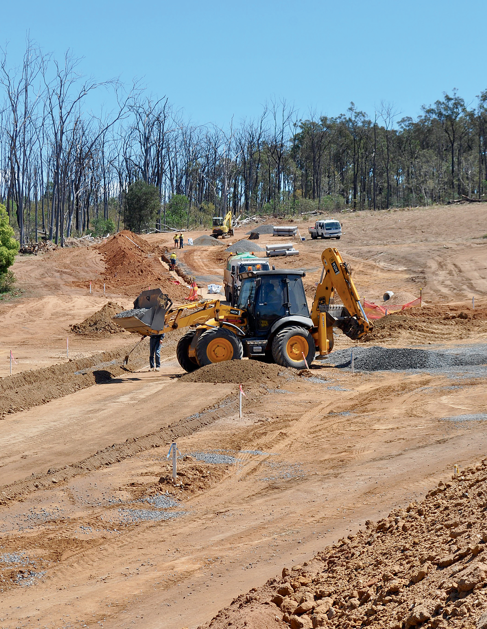 A photograph of road construction equipment digging roads and flattening areas of soil and gravel.