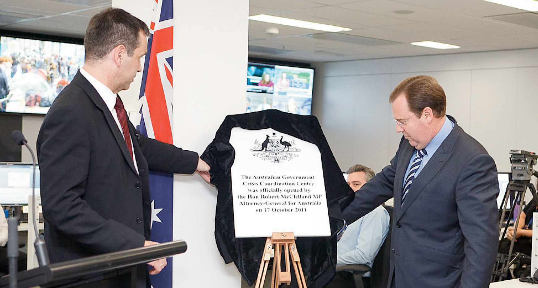 Photograph of the Hon Robert McClelland unveiling a plaque at the opening of the Crisis Coordination Centre, with CCC staff
