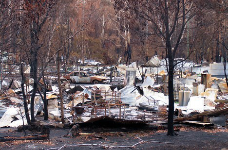 Photograph of destroyed houses and vehicles in a landscape after a fire