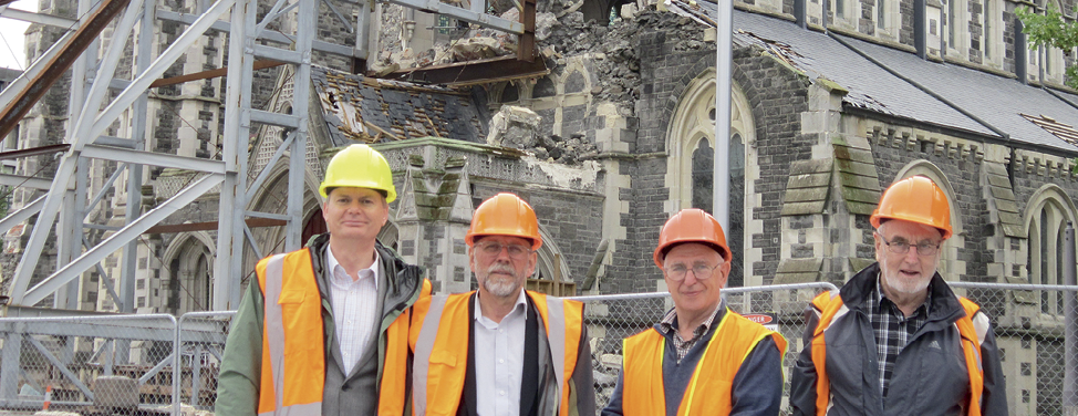 Photograph of four members of the Review Team in high-visibility vests and hard hats outside a damaged church