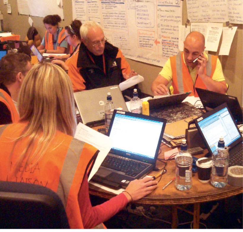Photograph of team members in high-visibility clothing at a table with laptops and phones