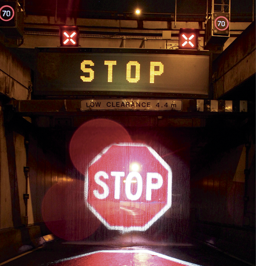 A road tunnel is closed off by a drop-down curtain and several different types of stop signs and warning lights.