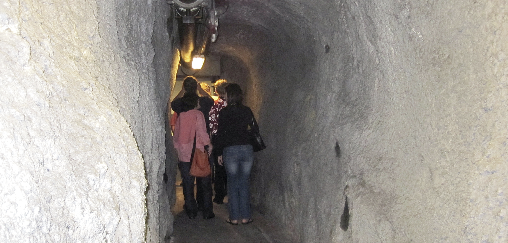 Photo of the inside of an exit cross-carriageway tunnel. The walls are roughly-hewn stone and there is a light overhead. Several adults are walking through the tunnel.