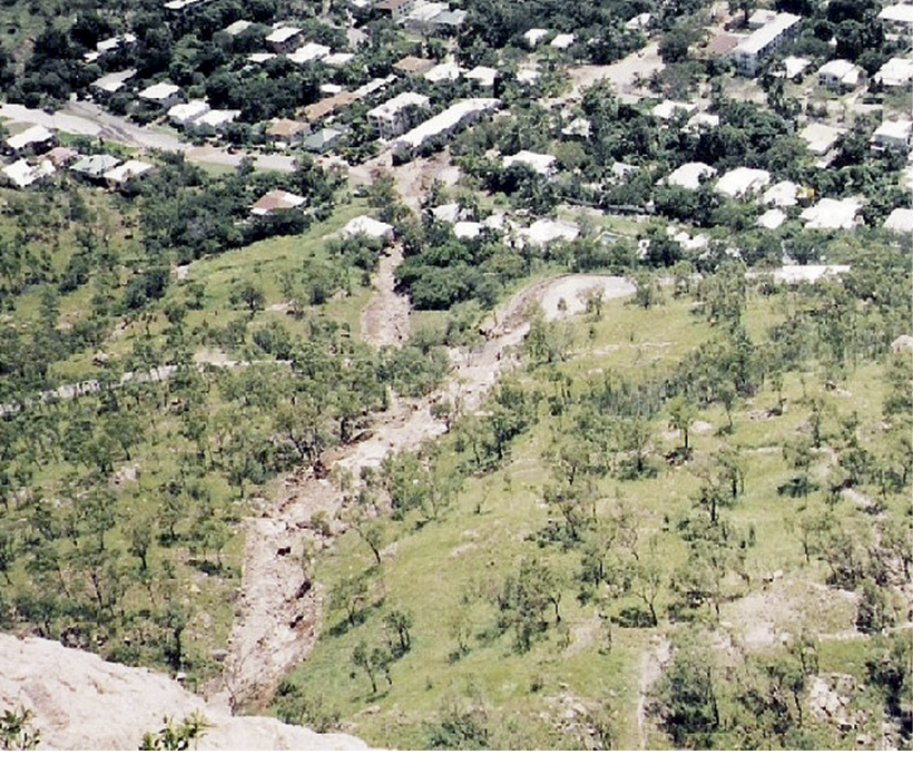 Aerial photo of a suburb at the bottom of a hillside with a wide muddy trail running down the hillside to the residential area.