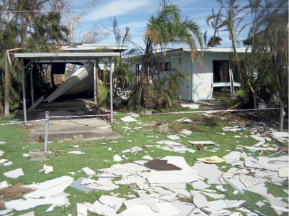 A single-storey house and carport has white sheets of asbestos debris covering the grassed yard.
