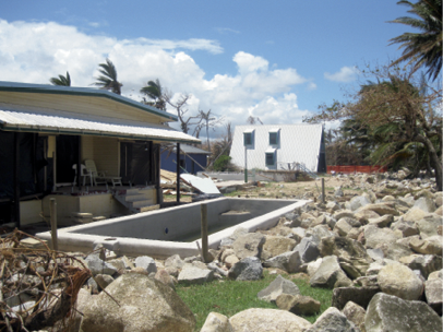A single-storey house has a half-empty inground swimming pool surrounded by large rocks.