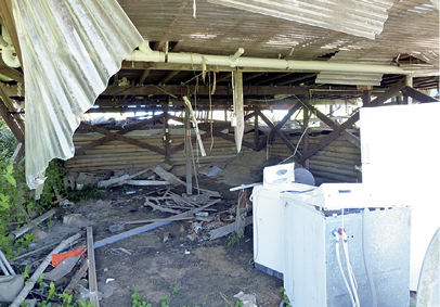 The interior of a large shed which is extensively damaged. There are some domestic washing machines and a fridge amongst the debris.