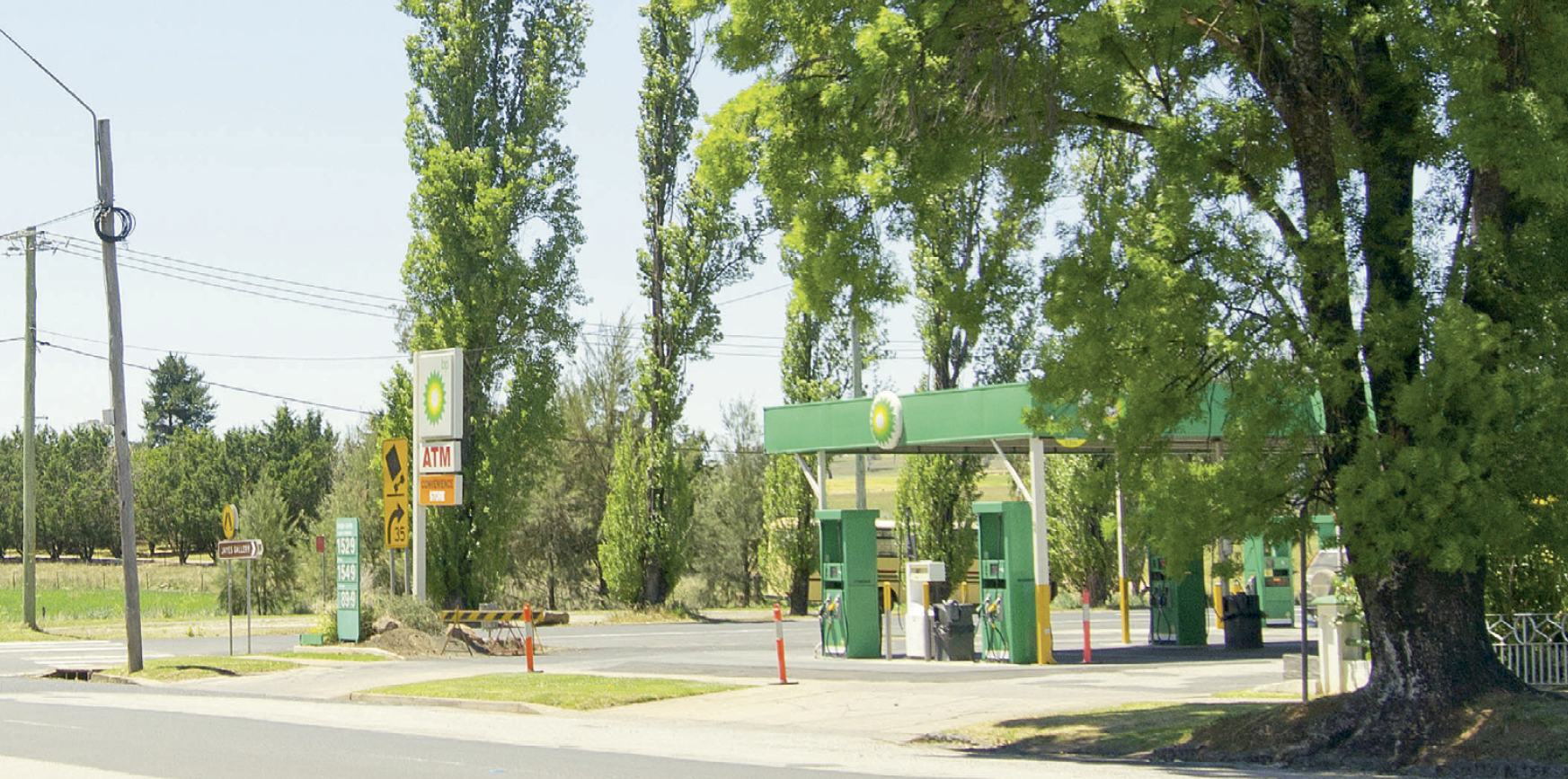 A BP petrol station surrounded by grassed areas and tall trees.