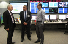 A visit to the Joint Earthquake and Tsunami Watch Centre at Geoscience Australia in Canberra with tsunami specialist Dr Andy Barnicoat and Centre Manager Dr Dan Jaksa. The men stand talking in the foreground with computer displays in the background.