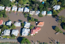 An aerial view of suburban houses surrounded by muddy floodwater such that the street itself is not visible.