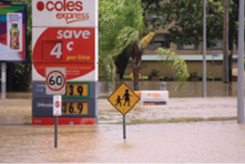 Muddy floodwaters cover the lower part of a large petrol station sign and nearby street signs.