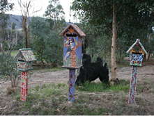 Colourfully decorated wooden letter boxes stand on posts beside a country road.