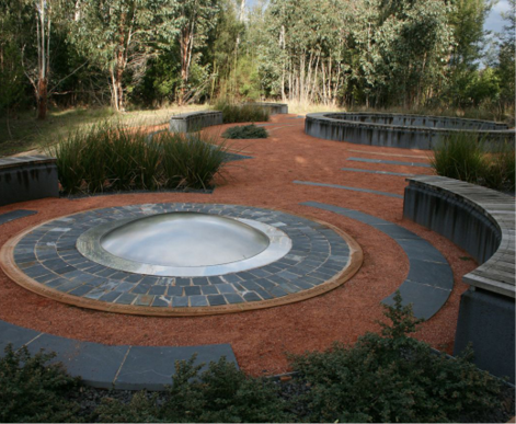 A landscaped garden with paved circles and benches in a forest clearing.