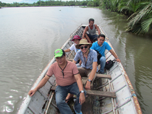 Michael Arman and four Phillipine adults sit in a wooden boat on a wide brown-water river with jungle along the banks.