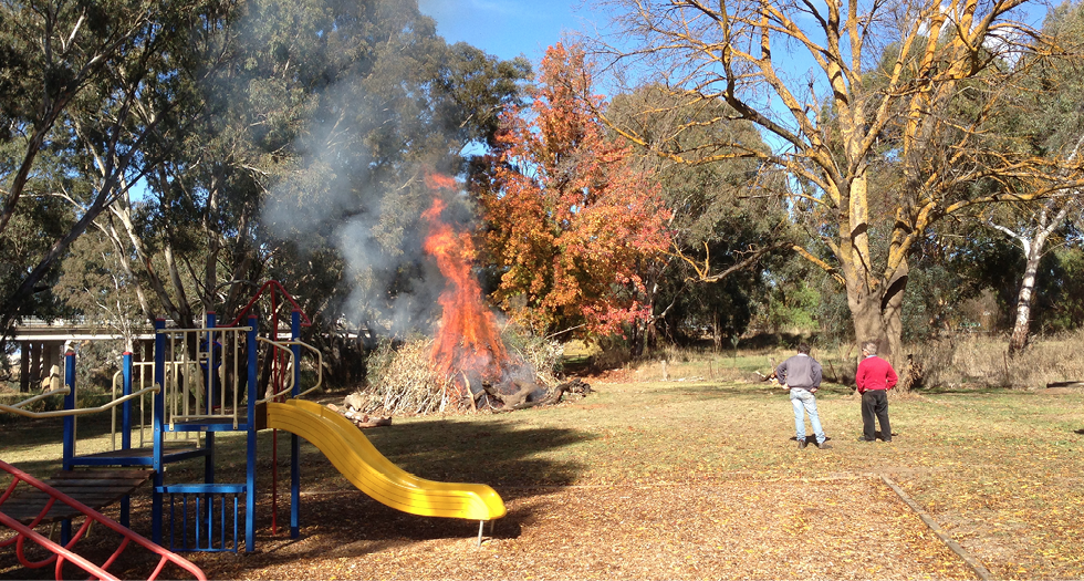 A photo of a park in Carisbrook, with play equipment in the foreground. In the background, residents tend a bonfire.
