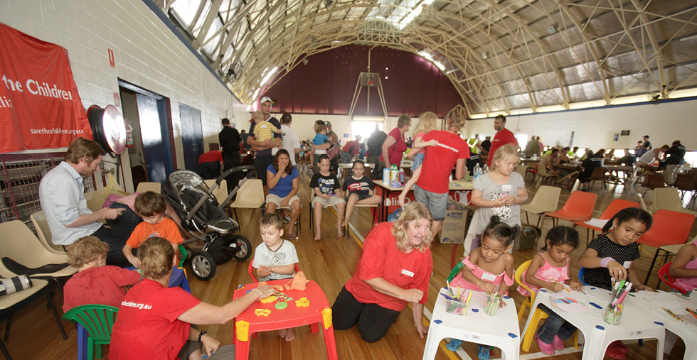 A photo of several children playing together indoors, along with adult supervisors.