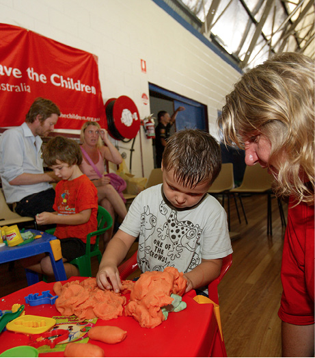 A photo of a child playing with play dough indoors, while being supervised by an adult.