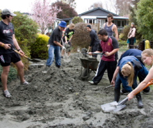 A photo of students helping with recovery efforts by shovelling mud in the front yard of a home.