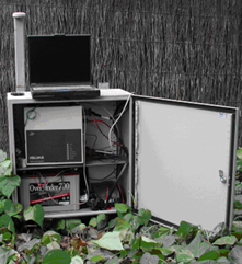 A photo of an earthquake recorder. It is a white metal cabinet that can be locked. The door is open, and inside is some equipment and cables. On top of the cabinet is a laptop.