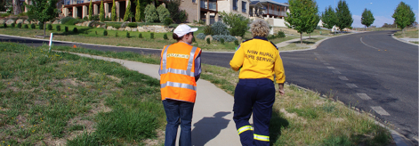 A photo of a female researcher and a female member of the NSW Rural Fire Service walking up a suburban street, with their backs towards us. 