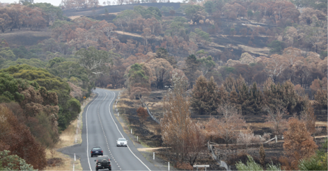 A photo of a highway running through rural properties among burnt bushland.