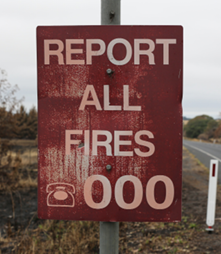 A photo of a partly fire-damaged emergency services sign, which reads ‘report all fires, 000’.