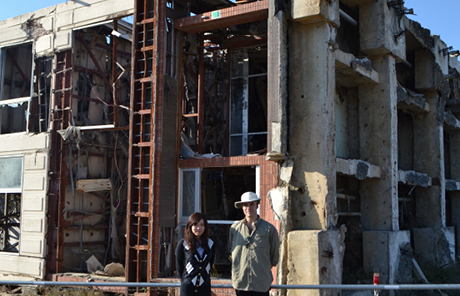 A young asian woman and a caucasian man are standing in front of a derelict multistory building.
