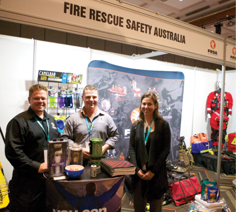 Two men and a woman are standing amid the Fire Rescue Safety Australia conference display of various safety equipment