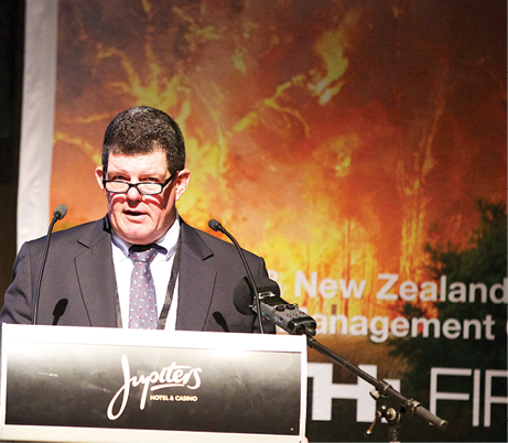 Deputy Commissioner Brett Pointing APM speaking from a lectern with an image of a bushfire in the background.