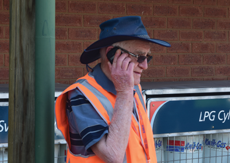 An elderly man wearing an orange safety vest is talking on a mobile phone.