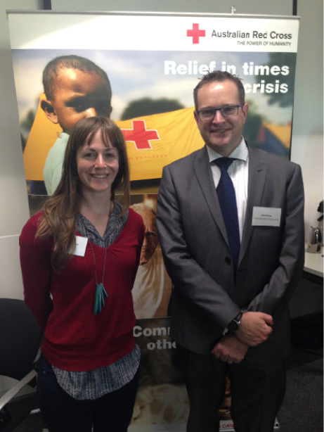 A young woman and man wearing office clothing are standing in front of an Australian Red Cross pull-up banner.